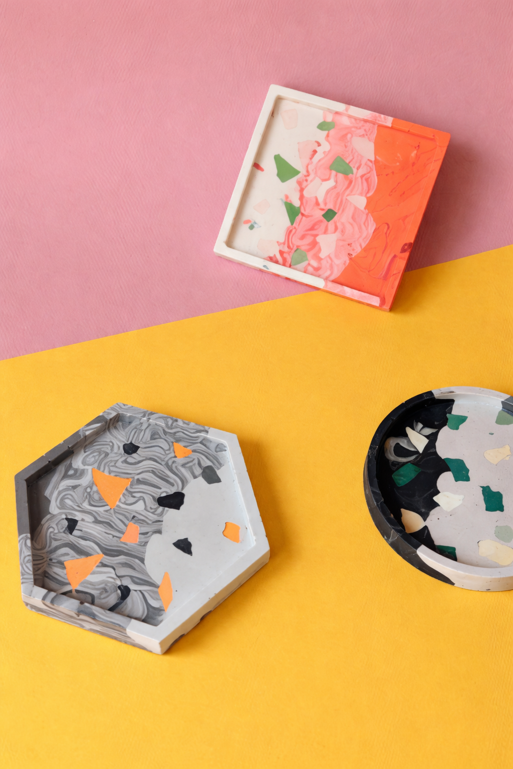Drie handgemaakte terrazzo resin schaaltjes op een roze en gele achtergrond